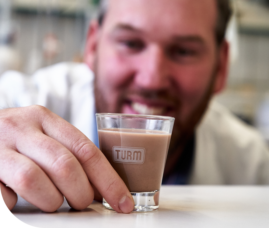 Kleines, mit Kakaogetraenk gefuelltes TURM-Glas wird hochgenommen von freundlichem Mann