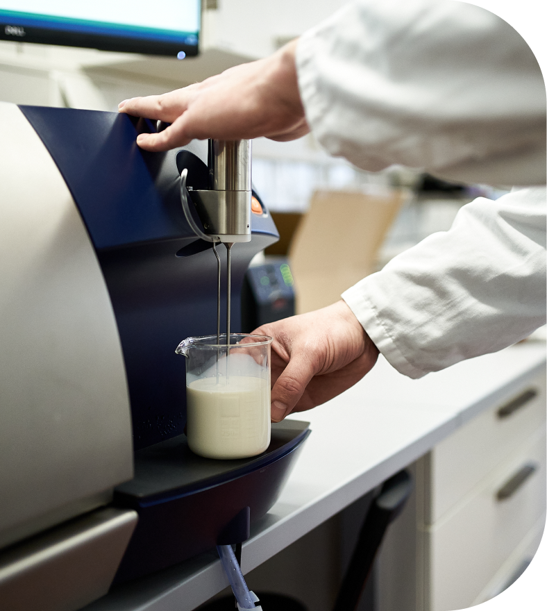 TURM Produktentwicklung Labormitarbeiter fuellt Becher an Automat mit Milchprodukt