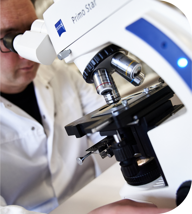 Labormitarbeiter in Kittel schaut durch Miskroskop